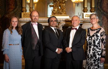 Group of people in front of an ornate fireplace, wearing evening wear and smiling towards the camera