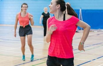 Woman in red top exercising in a sports hall