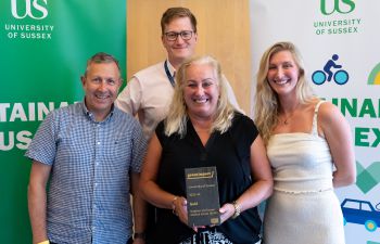 Members of the BSMS Green Impact team stood together with their recycled slate gold award in front of Sustainable Sussex banners