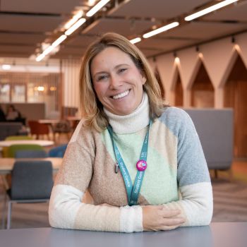 Photograph of Sarah smiling and leaning on a desk.