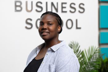 Cymone Geddes smiling and standing in front of Business School sign