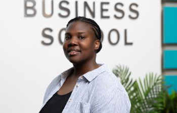 Cymone Geddes smiling and standing in front of Business School sign