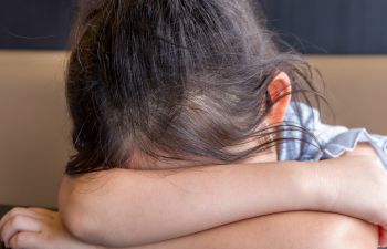 A child with dark hair resting their head in the arms on a table
