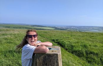 Zoe leans on a stone plinth in a green field