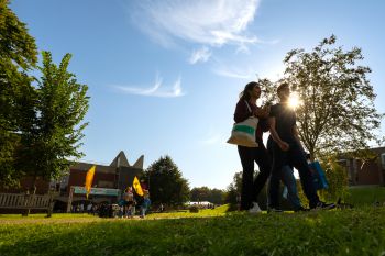 Students walking on campus with trees and buildings in the background