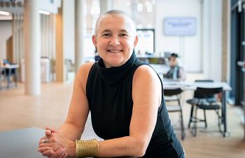 Kate O’Riordan, wearing a black sleeveless tshirt and a gold wrist cuff smiles at the camera.