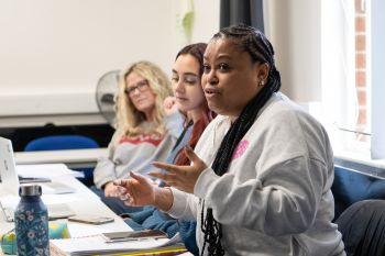 Three social work students are visible in this picture with the student closest to the camera - a black girl - being shown mid discussion. She uses her hands to emphasise the point she is making.