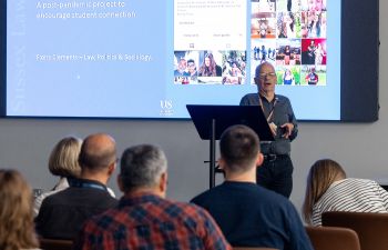 a man standing in front of a screen, which is showing text and pictures, with an audience in front of him