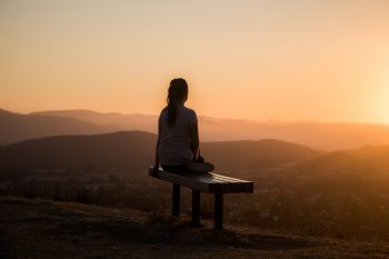 Person sat on bench looking at a calming landscape of hills and mountains