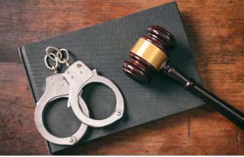 Handcuffs and gavel placed on a black book on a wooden table