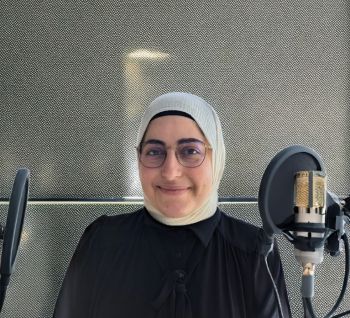 headshot of woman wearing headscarf and black dress, with podcast mics