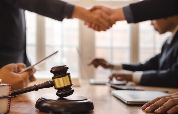 Blurred image of board meeting desk with people sitting and standing around it with gavel in the middle two people shaking hands across the table