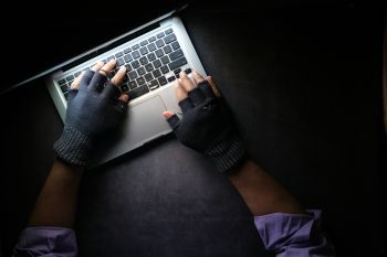 A pair of gloved hands hover over a keyboard in a darkened space
