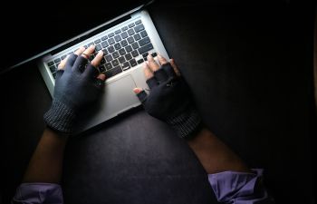 A pair of gloved hands hover over a keyboard in a darkened space