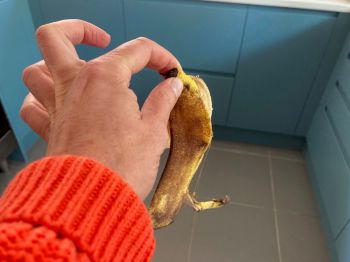 A hand holding a banana skin: she is wearing an orange cardigan and blue cupboards are visible