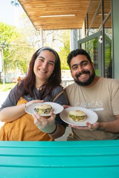 Women holding an arepa, a white flatbread filled with black beans and vegan cheese and a man holding an arepa, filled with chicken and avocado