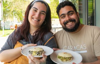 Women holding an arepa, a white flatbread filled with black beans and vegan cheese and a man holding an arepa, filled with chicken and avocado