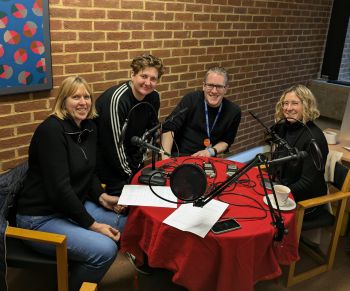 A photograph of four people sitting at a round table, which has microphones and other podcast equipment on it
