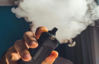 A close up of someone vaping with a cloud of smoke above their fingers