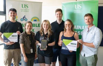 The Life Sciences Green Impact team standing together, smiling and holding their awards in front of sustainability banners