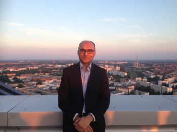 Prof Anjum Memon of BSMS pictured outside in front of a sunset sky in a suit jacket