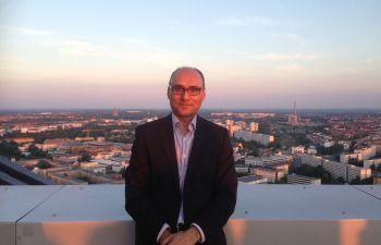 Prof Anjum Memon of BSMS pictured outside in front of a sunset sky in a suit jacket
