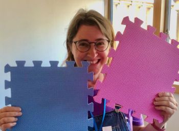 Katie Piatt smiling at the camera holding large purple and pink jigsaw pieces