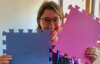Katie Piatt smiling at the camera holding large purple and pink jigsaw pieces