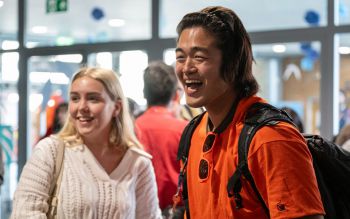 two smiling students, one is wearing an orange tshirt and the other has blonde hair