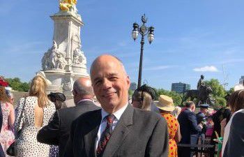 Professor David Ruebain smiling at the camera in front of a fountain outside Buckingham Palace