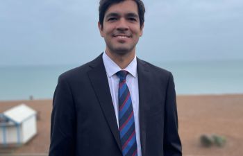 Sebastian Rodrigues, smiling at the camera in a suit with Brighton beach in the background