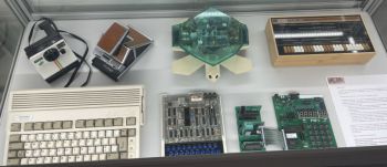 various old tech including Polaroid camera and keyboard inside glass case