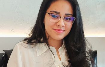 A portrait photo of a student with long, dark hair wearing glasses in front of a white background.