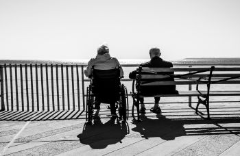 A black and white photo of an elderly couple sat on a bench with their backs to the camera
