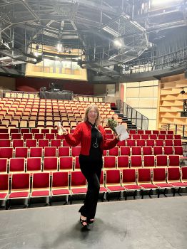 Hannah standing on the stage and holding a bouquet of flowers and a bottle of champagne