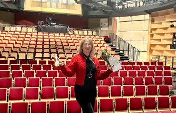 Hannah standing on the stage and holding a bouquet of flowers and a bottle of champagne
