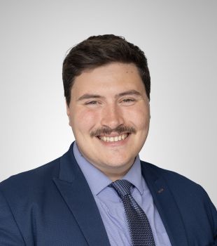 An official portrait photograph of a smiling Tom Rylatt wearing a smart blue suit and tie