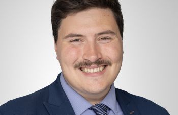 An official portrait photograph of a smiling Tom Rylatt wearing a smart blue suit and tie
