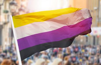 A non-binary flag flies from a flag pole