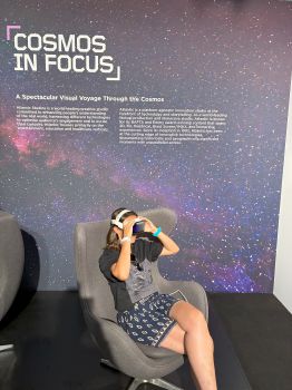 A girl seated in a chair wearing a headset, facing an exhibit sign labeled