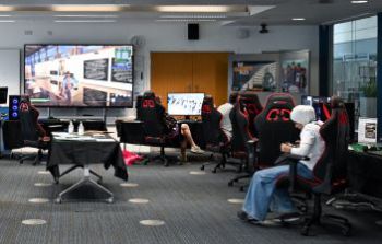 People in a gaming room playing a video game on multiple monitors and a large screen
