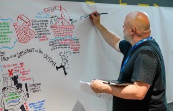 Person drawing on a whiteboard filled with colourful sketches, notes, and quotes