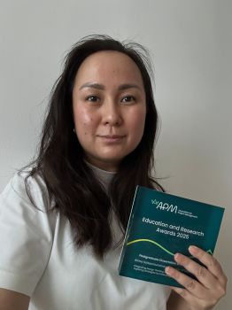 Head shot of woman with long dark hair holding her dissertation