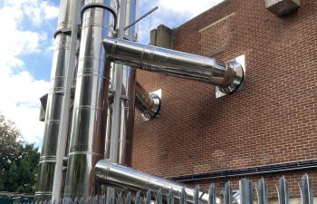 Silver pipes going into a brick building for heating