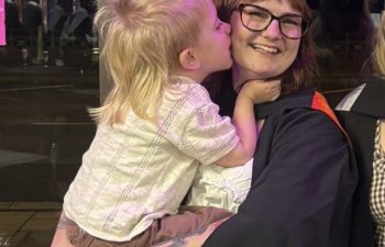 Rhiannon Williams is shown wearing her graduation robe grinning and holding her young son at her graduation ceremony in 2024