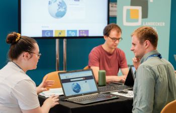 Attendees in a discussion sat around a table with a laptop at the Connective Holocaust Commemoration Expo 2025.