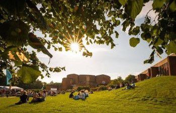Campus view with people sitting on grass in front of the library