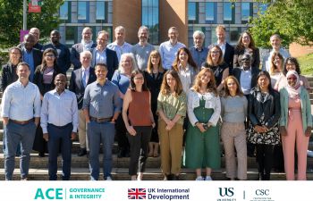 Male and female researchers standing together looking at the camera in front of the Sussex Business School