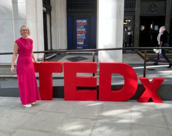 Prof Claire Smith next to the TED x NHS red lettering outside a building