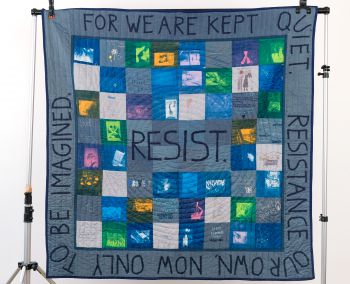 A photograph of a blue patchwork quilt made during a workshop on Imagining Resistance.
